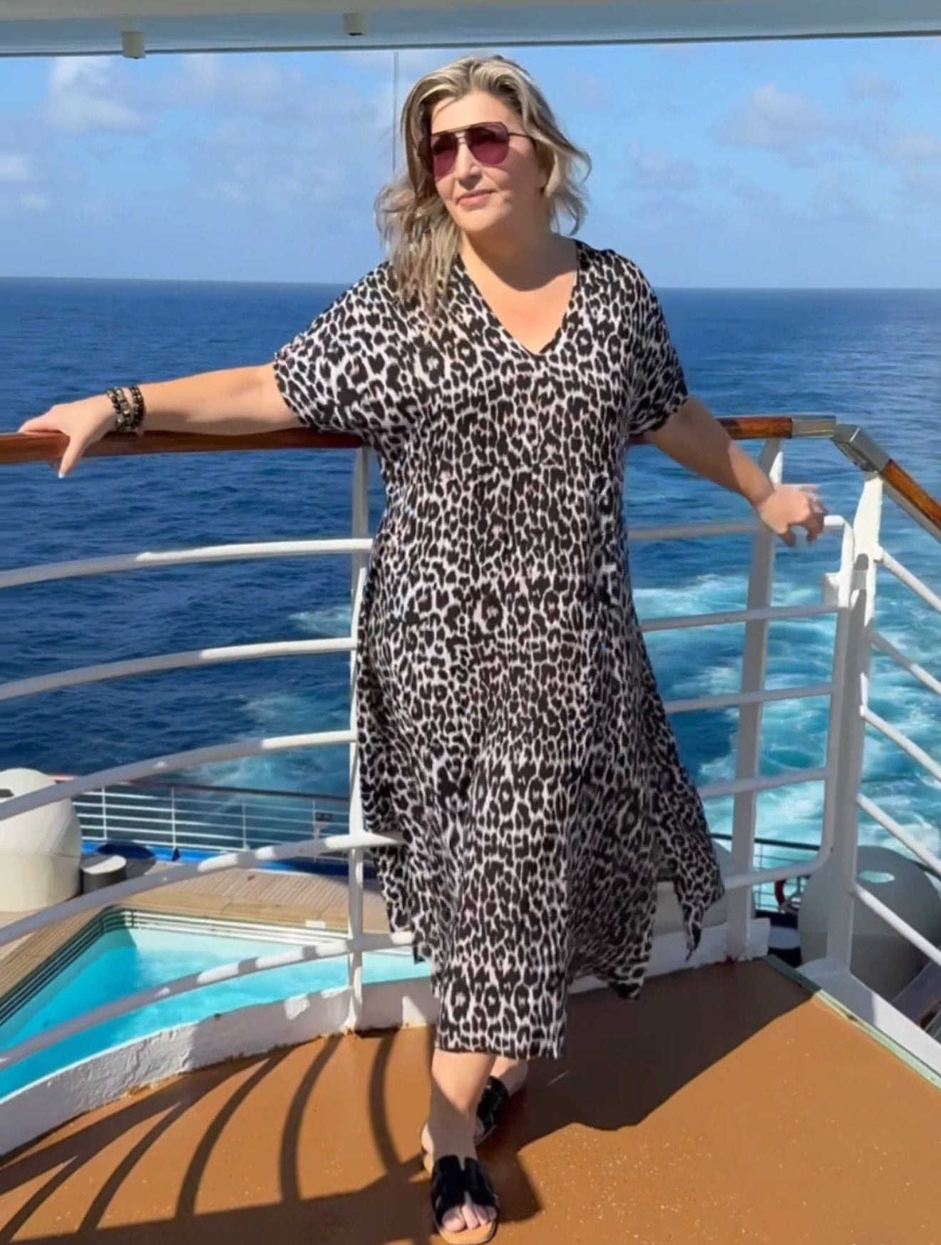 Woman in a long leopard print dress standing on a cruise ship deck with ocean view