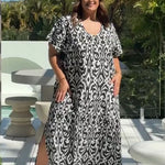 Woman wearing a black and white patterned dress standing on outdoor deck with greenery in the background