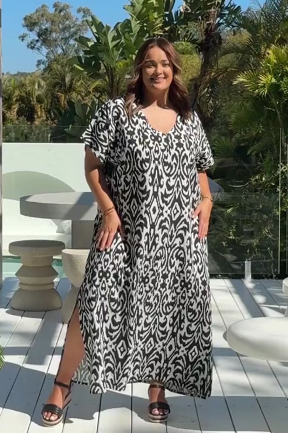 Woman wearing a black and white patterned dress standing on outdoor deck with greenery in the background