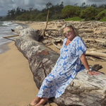 woman wearing long kaftan dress in blue and white floral while sitting at the beach