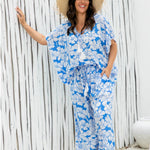 Woman wearing a blue floral pants with matching summer top against a white wooden fence of beach resort