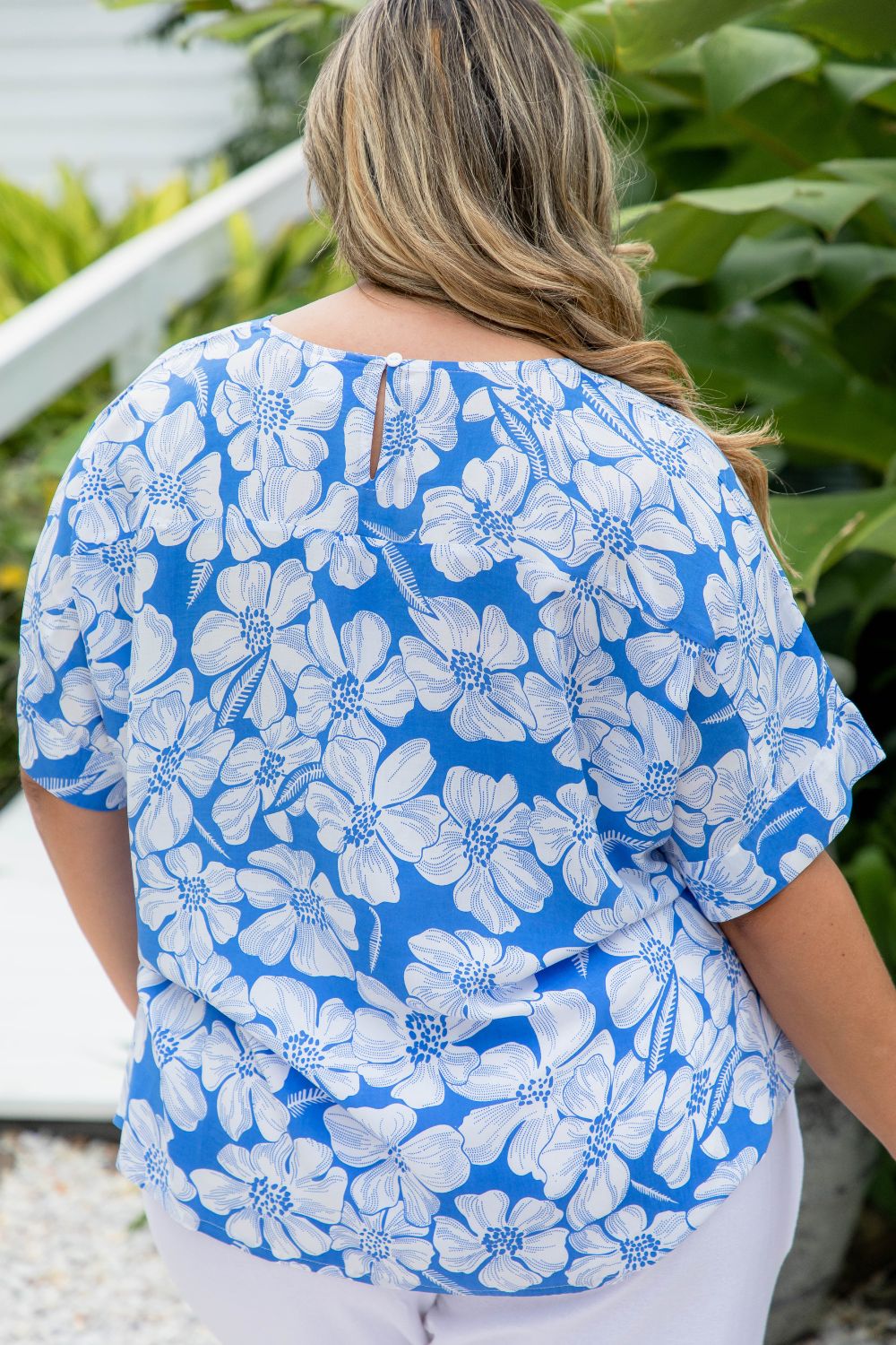 Woman wearing a blue and white floral blouse with a garden background