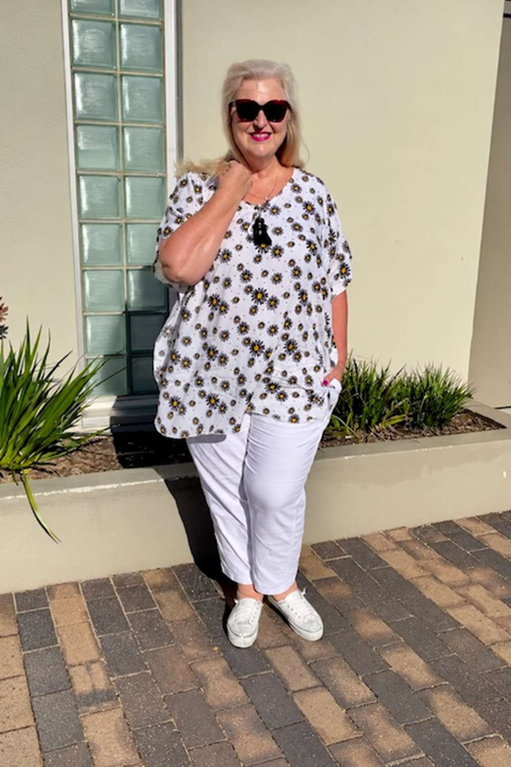 Jacqui from New Style Chapters wearing the White Daisy kaftan top with black and yellow daisies, styled with white pants.