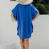 Back view of Alisha wearing the Lagoon Blue short kaftan dress in size SM, with a woven hat and cream sandals.