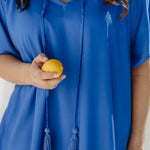 Close-up of the Lagoon Blue kaftan's V-neckline and matching cotton tassel ties, with Alisha holding a lemon.