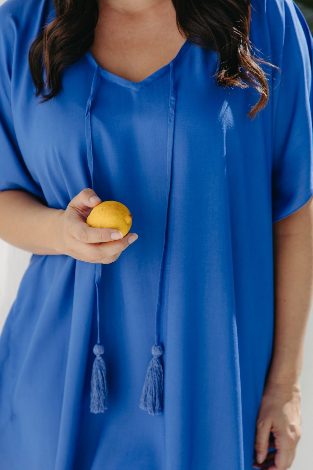 Close-up of the Lagoon Blue kaftan's V-neckline and matching cotton tassel ties, with Alisha holding a lemon.