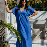 Front view of the Lagoon Blue long kaftan dress worn loose without a belt on a sunny deck with tropical foliage.