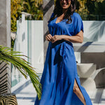 Lagoon Blue long kaftan dress with matching belt, showing the side split as the model steps forward on a sunny deck.
