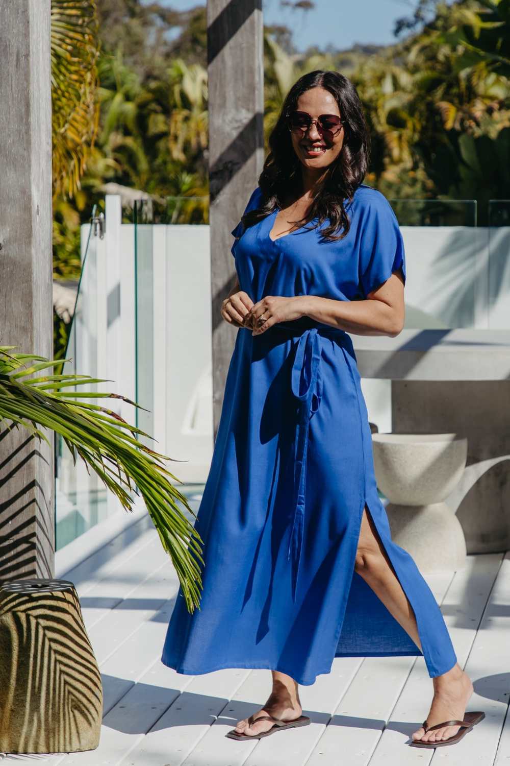 Lagoon Blue long kaftan dress with matching belt, showing the side split as the model steps forward on a sunny deck.