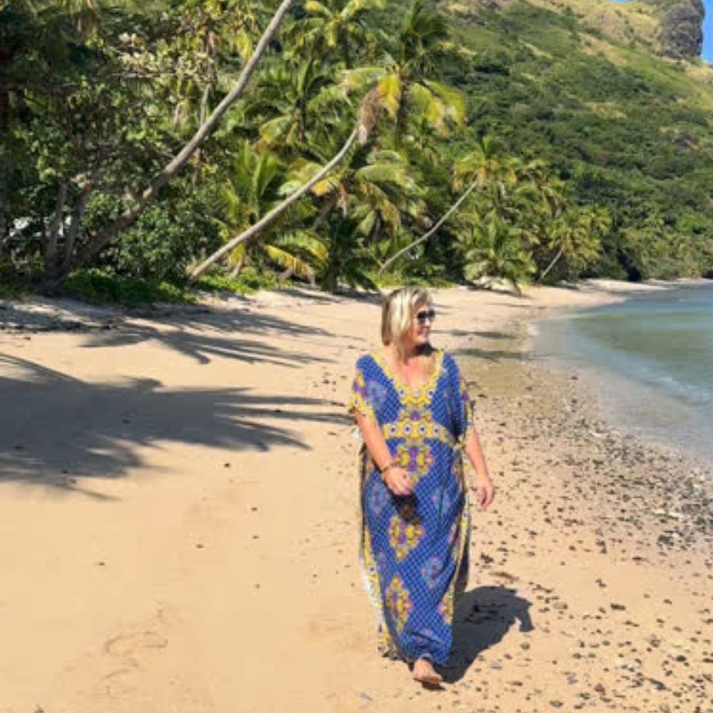 Lady wearing long kaftan dress while strolling along beach in Fiji on holiday