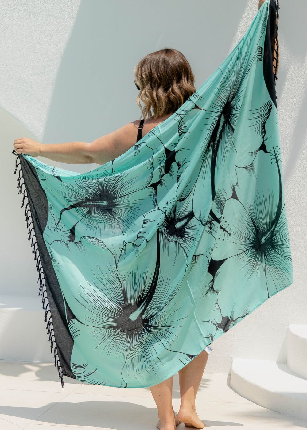 Woman poolside holding a mint green Hawaiian sarong with black hibiscus flower details 