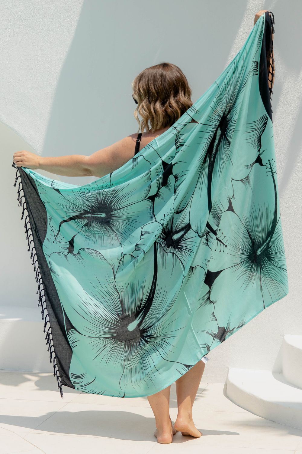 Woman poolside holding a mint green Hawaiian sarong with black hibiscus flower details 