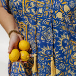 Person wearing a blue and yellow patterned dress holding lemons - the limoncello print