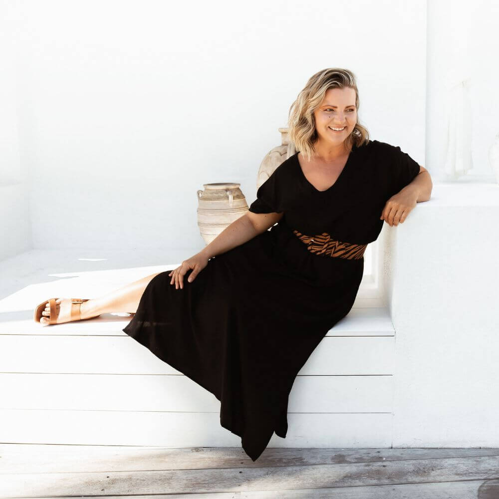 Mature model wearing black A-line maxi resort dress seated on outdoor deck bench