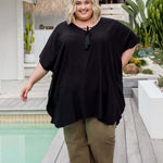 Plus size model walking poolside wearing a black kaftan top with relaxed fit and fluid movement