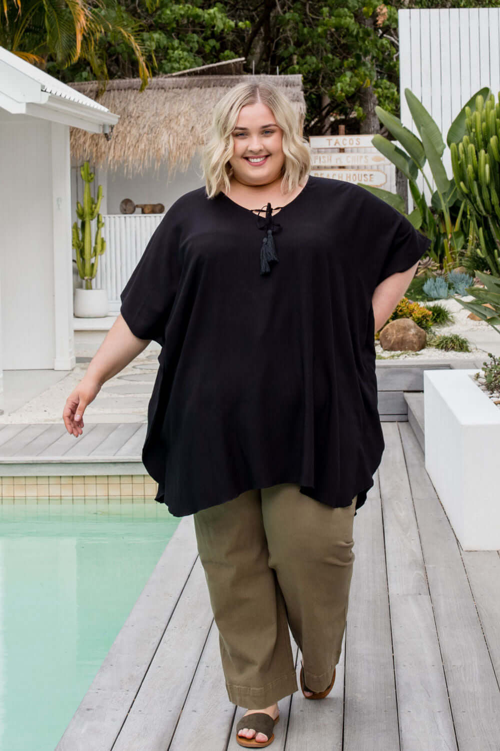 Plus size model walking poolside wearing a black kaftan top with relaxed fit and fluid movement