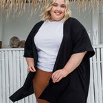 Plus size model wearing black kimono cape layered over wide leg pants