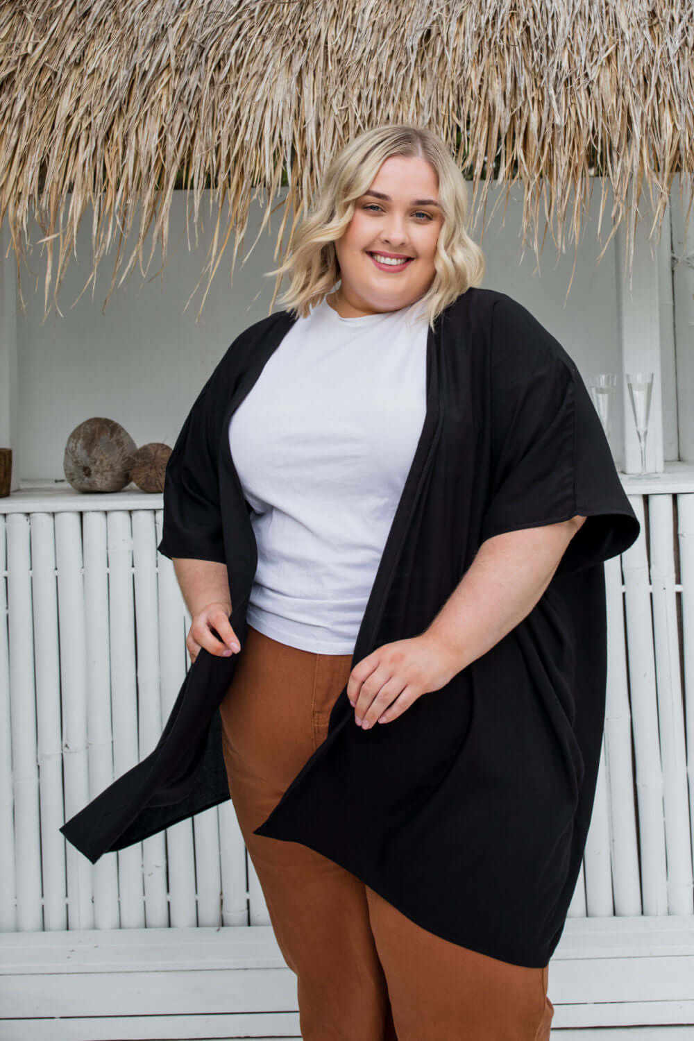 Plus size model wearing black kimono cape layered over wide leg pants