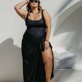 Woman in an extra large  black sarong standing by a poolside.