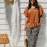 Alisha in Mocha Mousse Kaftan Top size S/M leaning against deck wall with sun hat and sarong in background, styled with leopard pants