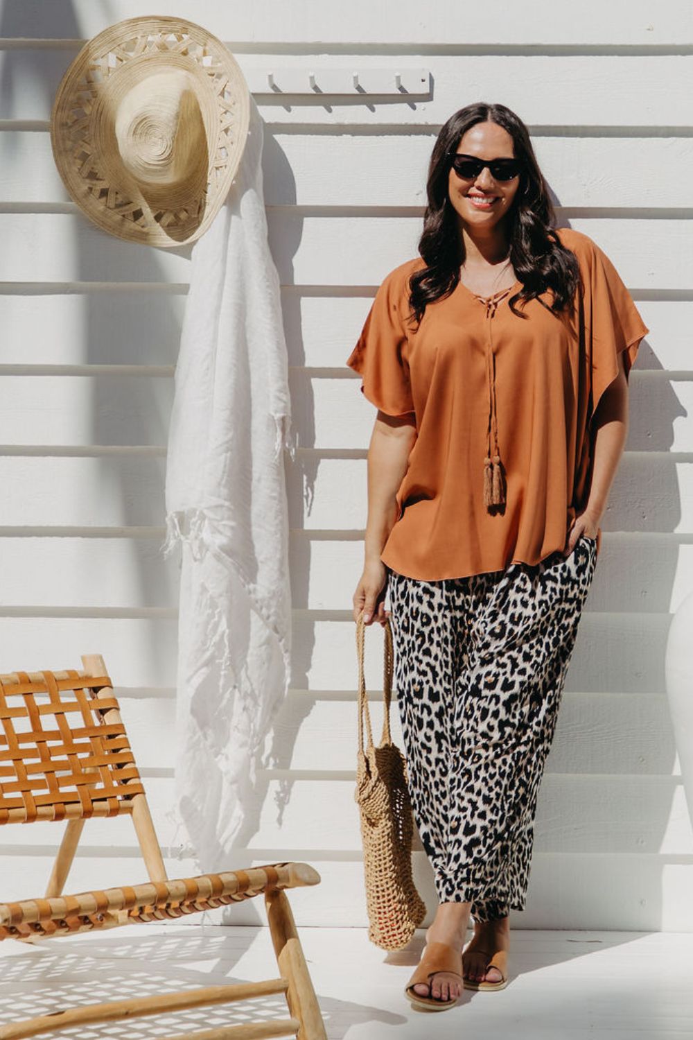 Alisha in Mocha Mousse Kaftan Top size S/M leaning against deck wall with sun hat and sarong in background, styled with leopard pants