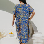 Woman wearing a blue and yellow print maxi dress standing against a white wall in Italian villa setting