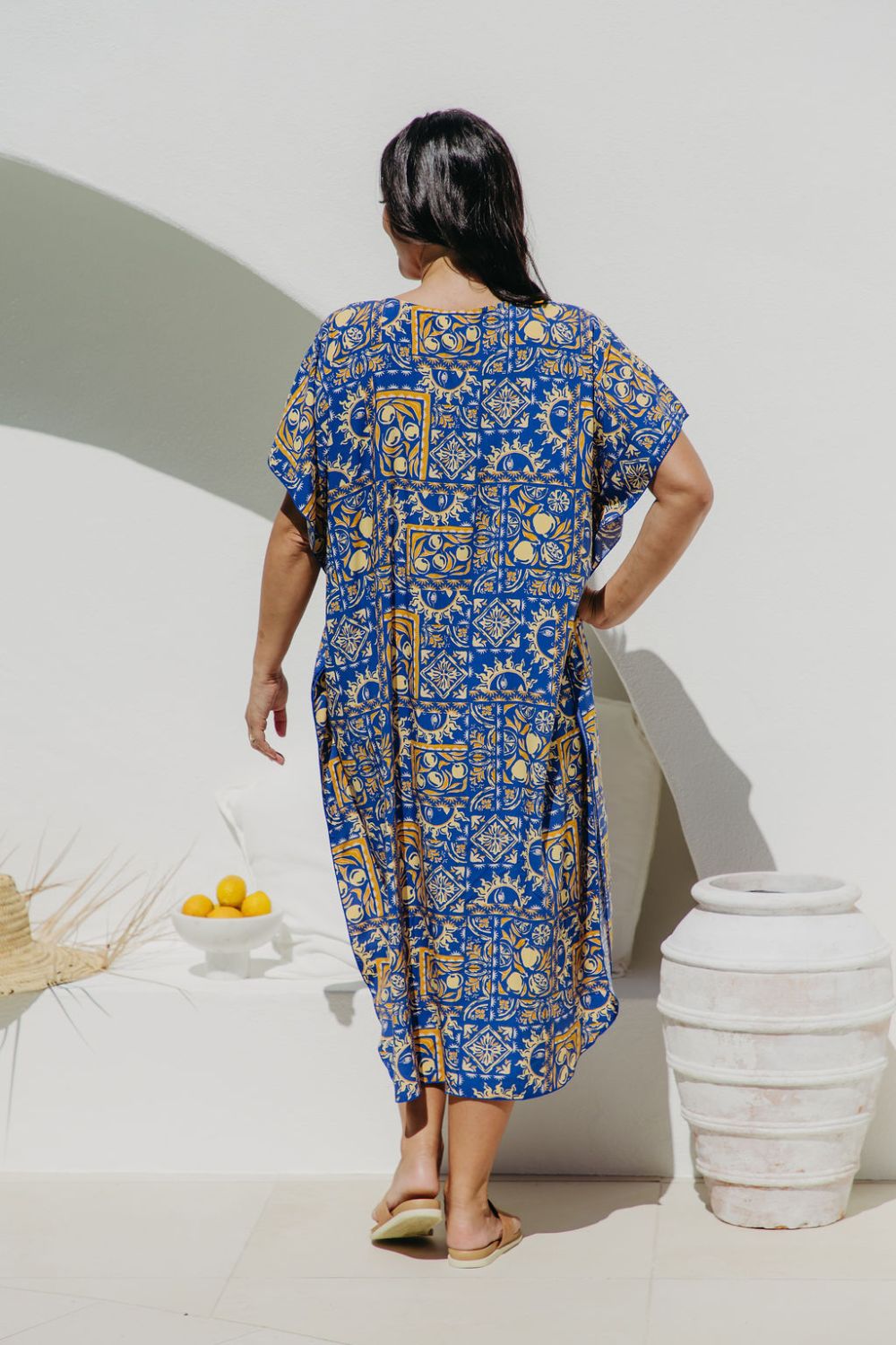 Woman wearing a blue and yellow print maxi dress standing against a white wall in Italian villa setting