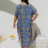 Woman wearing a blue and yellow print maxi dress standing against a white wall in Italian villa setting