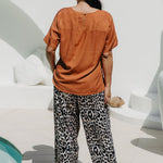 Lady wearing a caramel brown coloured top and leopard print pants standing in a sunlit area in the pool entertaining area