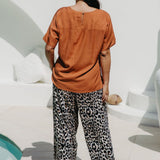Lady wearing a caramel brown coloured top and leopard print pants standing in a sunlit area in the pool entertaining area