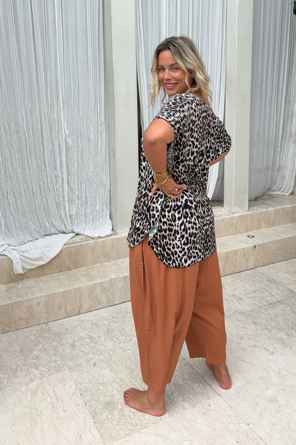 Back view tropical travel outfit set of  leopard kaftan and mocha wide-leg pants outfit being worn poolside in Canggu, Bali villa on summer holiday