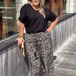 Woman wearing a black top and leopard print pants standing on a wooden deck.