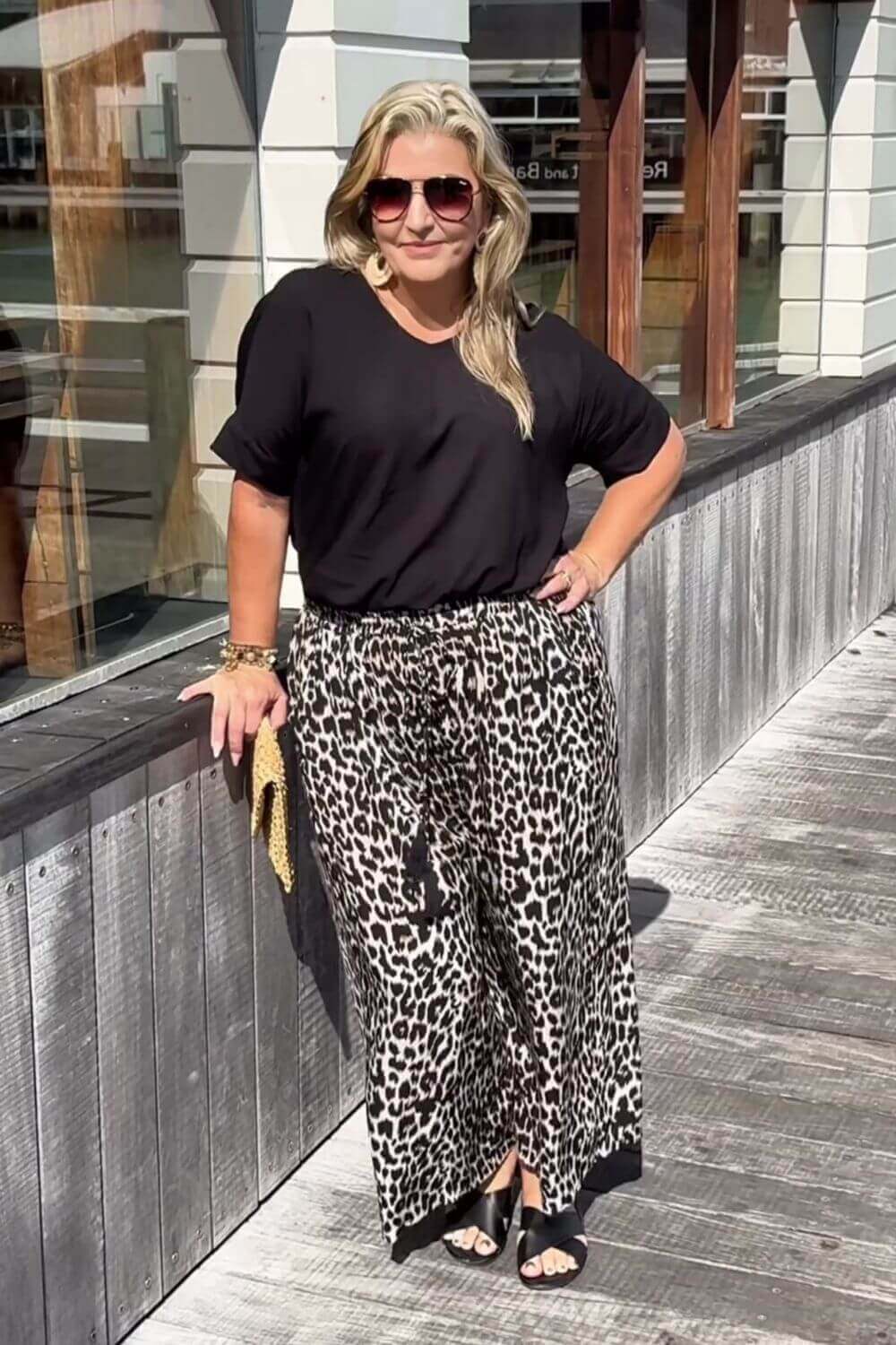 Woman wearing a black top and leopard print pants standing on a wooden deck.
