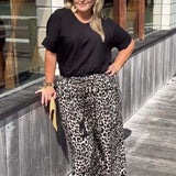 Woman wearing a black top and leopard print pants standing on a wooden deck.