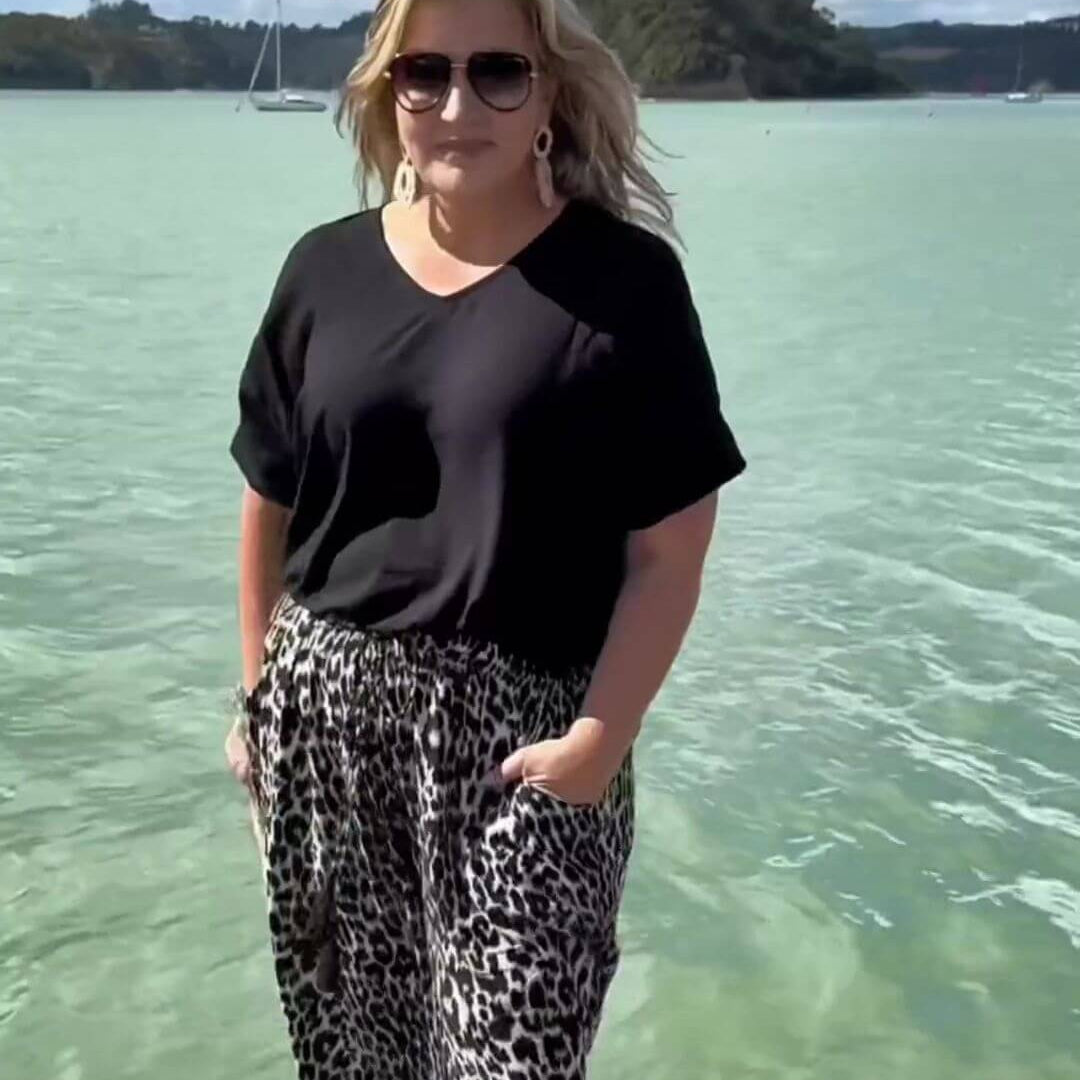 Mature woman wearing black summer blouse top with wide leg leopard print pants whilst on holiday in New Zealand