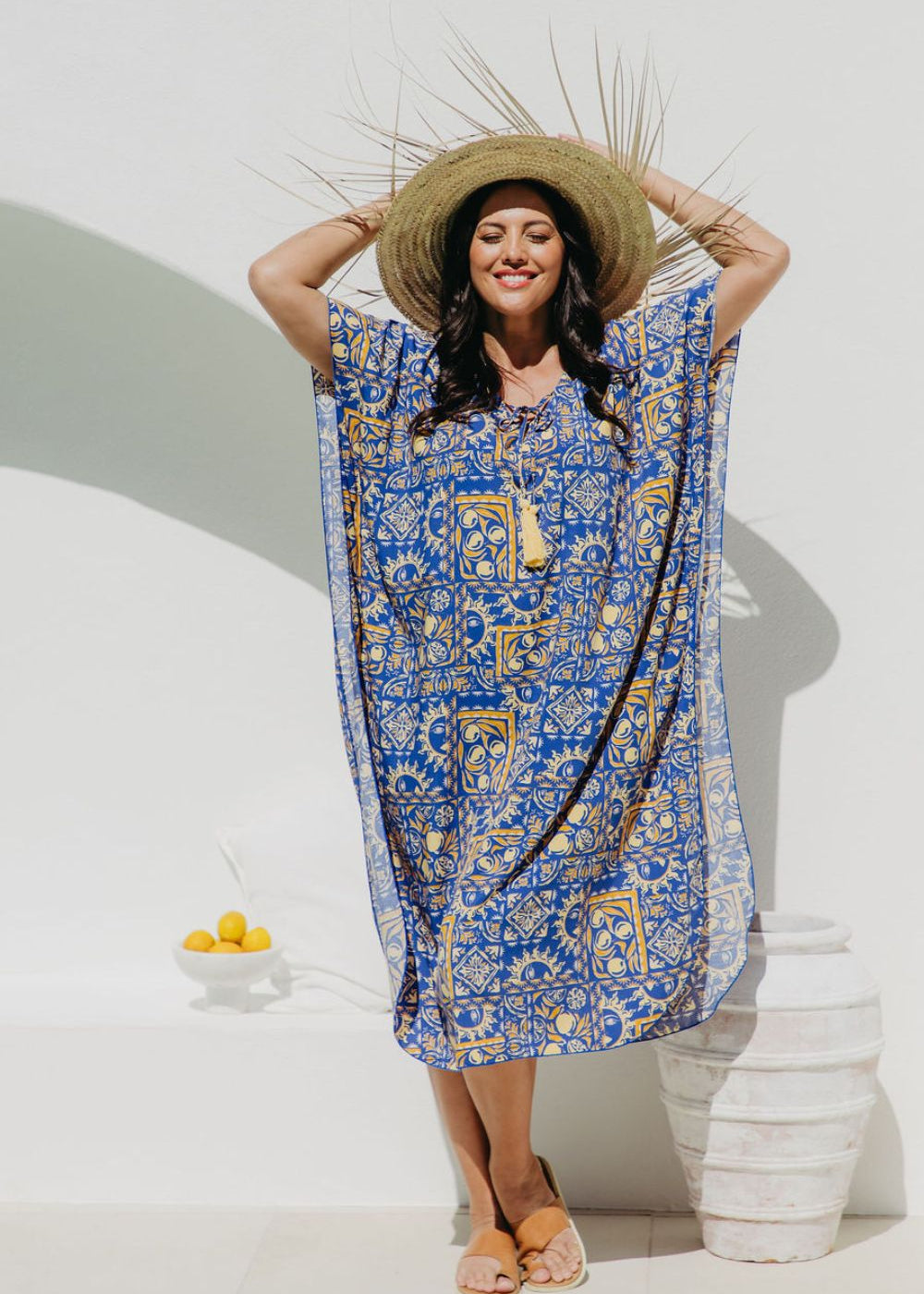 Woman wearing a blue and yellow Positano inspired print designed kaftan dress and straw hat in Italian seaside resort