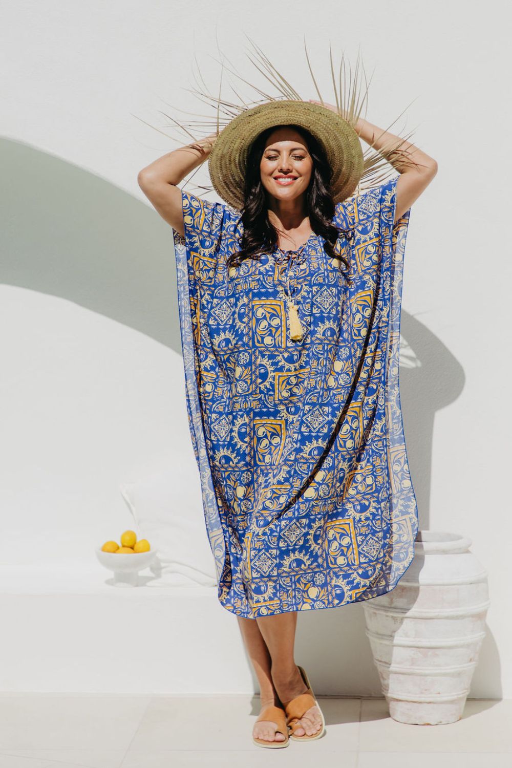 Woman wearing a blue and yellow Positano inspired print designed kaftan dress and straw hat in Italian seaside resort