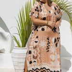 A woman models a peach-colored maxi kaftan dress with a black and white geometric pattern, standing in front of a white wall with a potted palm plant.