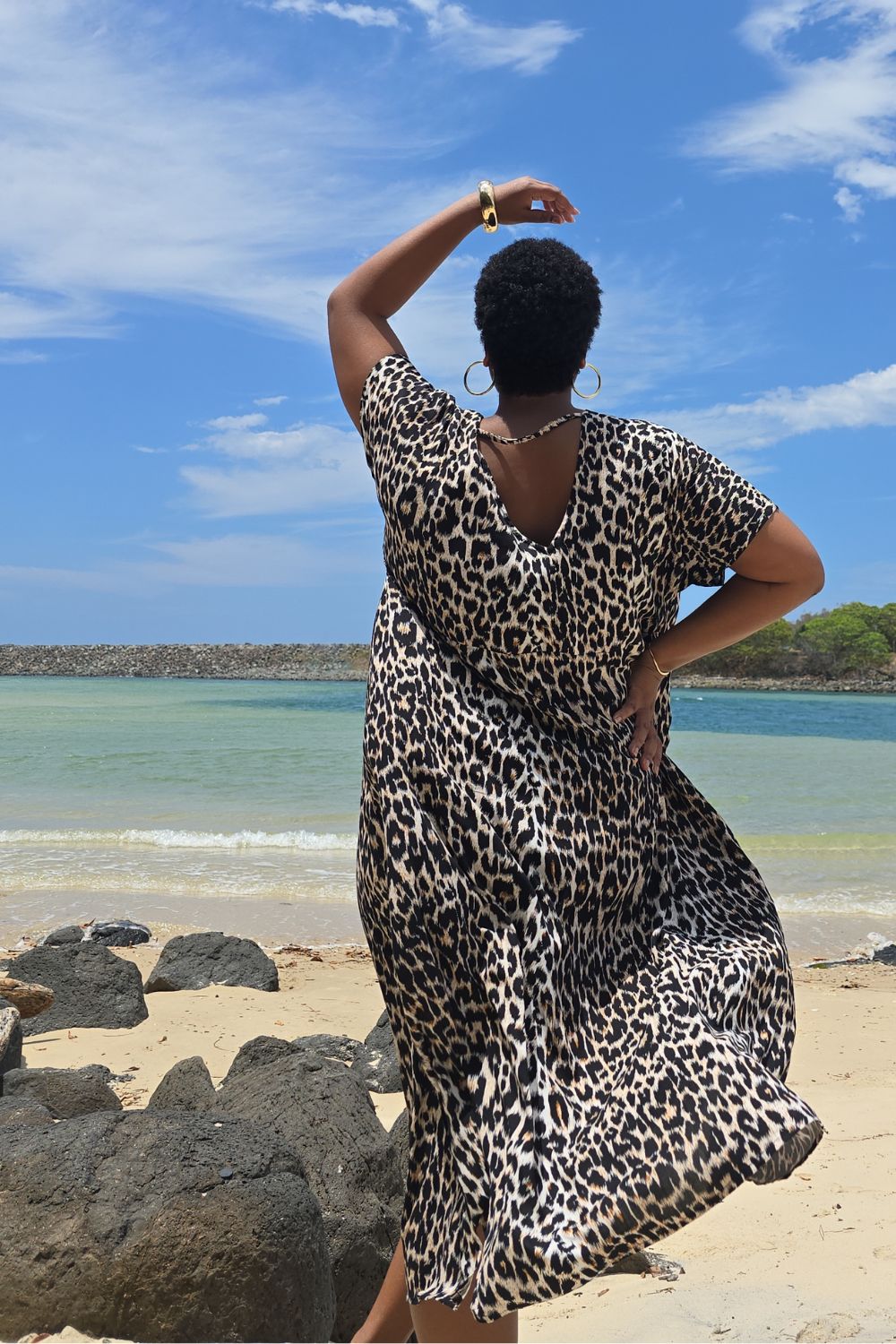 Woman wearing a leopard print dress standing on a Sunshine Coast beach in Queensland with a blue sky and ocean in the background.