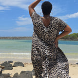Woman wearing a leopard print dress standing on a Sunshine Coast beach in Queensland with a blue sky and ocean in the background.