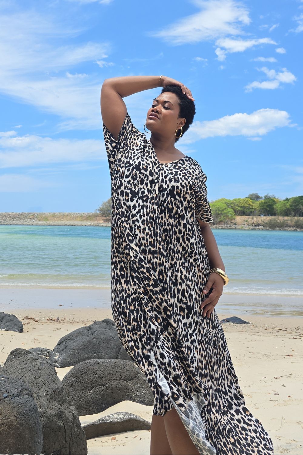 Woman in a leopard print dress standing on a Sunshine Coast beach with blue sky and water in the background