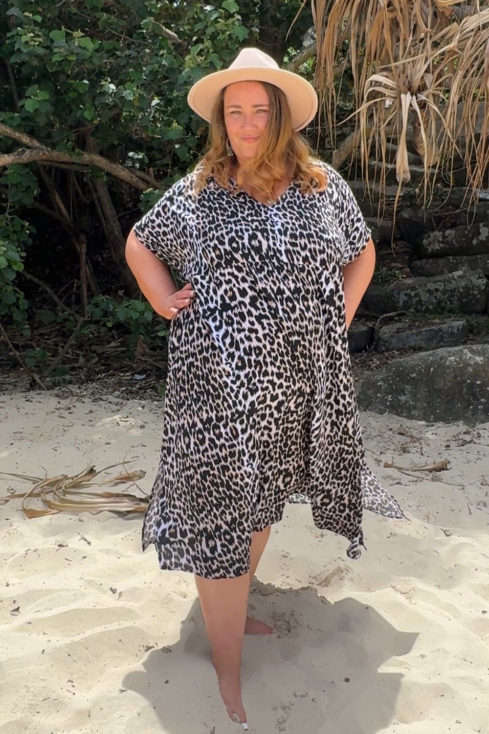 Woman in a leopard print dress and hat standing on a sandy beach at the Gold Coast Australia