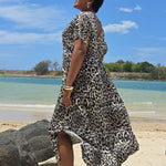 Woman in a leopard print dress standing on a Queensland beach with a blue sky and water in the background