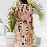 A woman stands with her back to the camera wearing a antique brass maxi kaftan dress with a black and ghost white abstract tribal pattern. She is holding a straw hat and standing in front of a white wall with a potted palm plant.