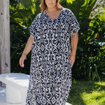 Woman wearing a black and white patterned dress in long summer style standing outdoors with greenery in the background