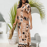 A mature woman modelling a soft terracotta maxi dress with black and ghost white geometric and botanical patterns, standing in a outdoor area poolside with potted palm behind