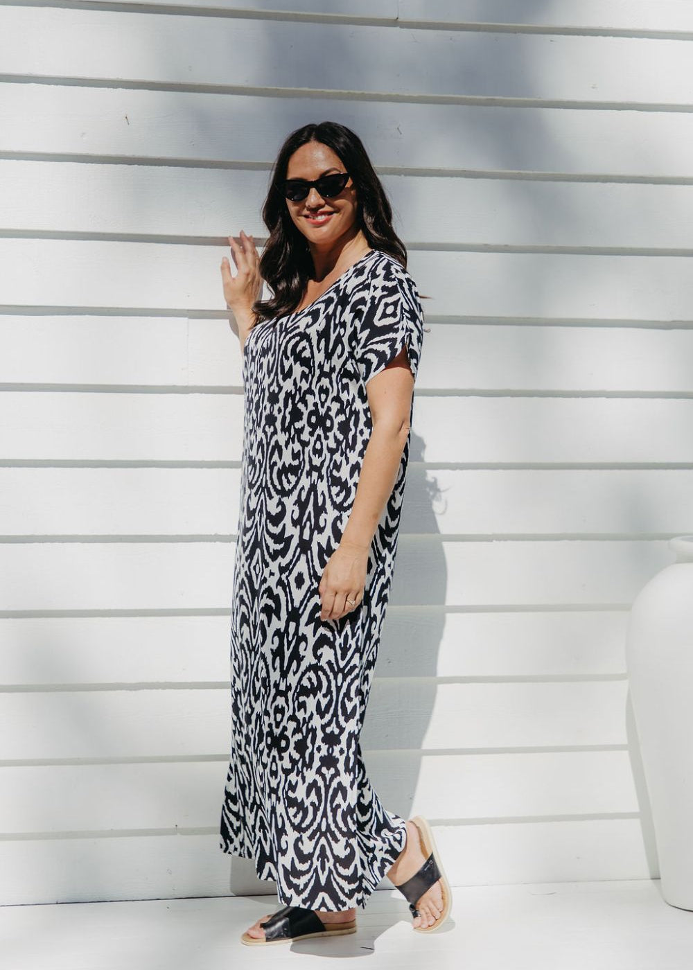 Lady wearing long summer dress in black and white geometric print relaxing on the outdoor patio in filtered summer sun