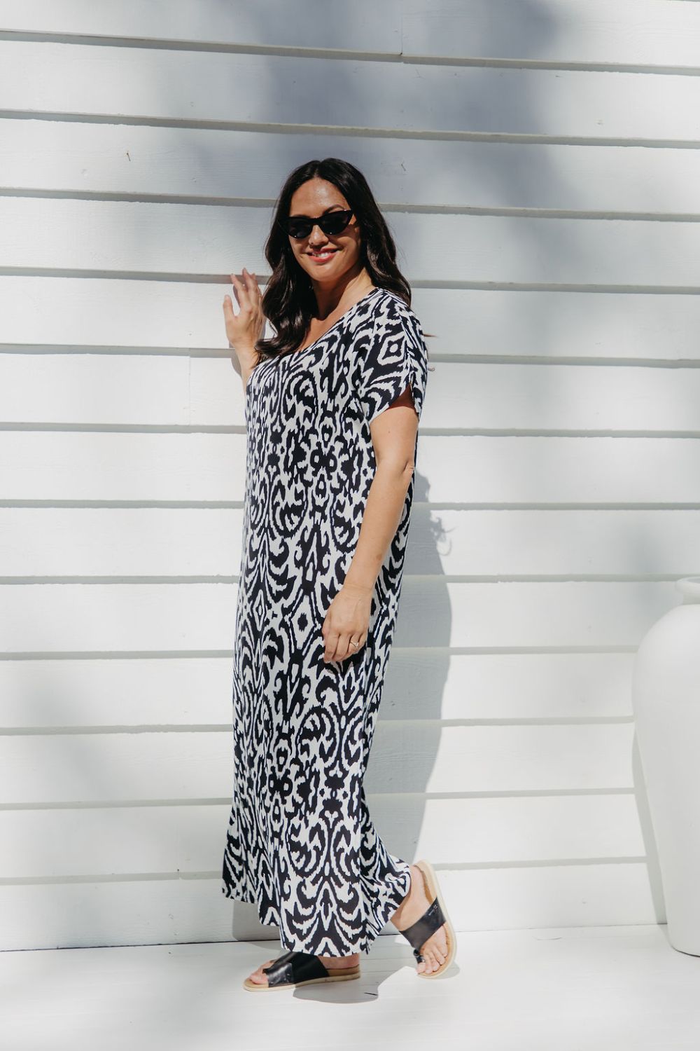 Lady wearing long summer dress in black and white geometric print relaxing on the outdoor patio in filtered summer sun