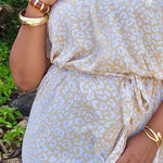 Woman wearing a beige and white leopard print long summer dress with gold accessories outdoors.