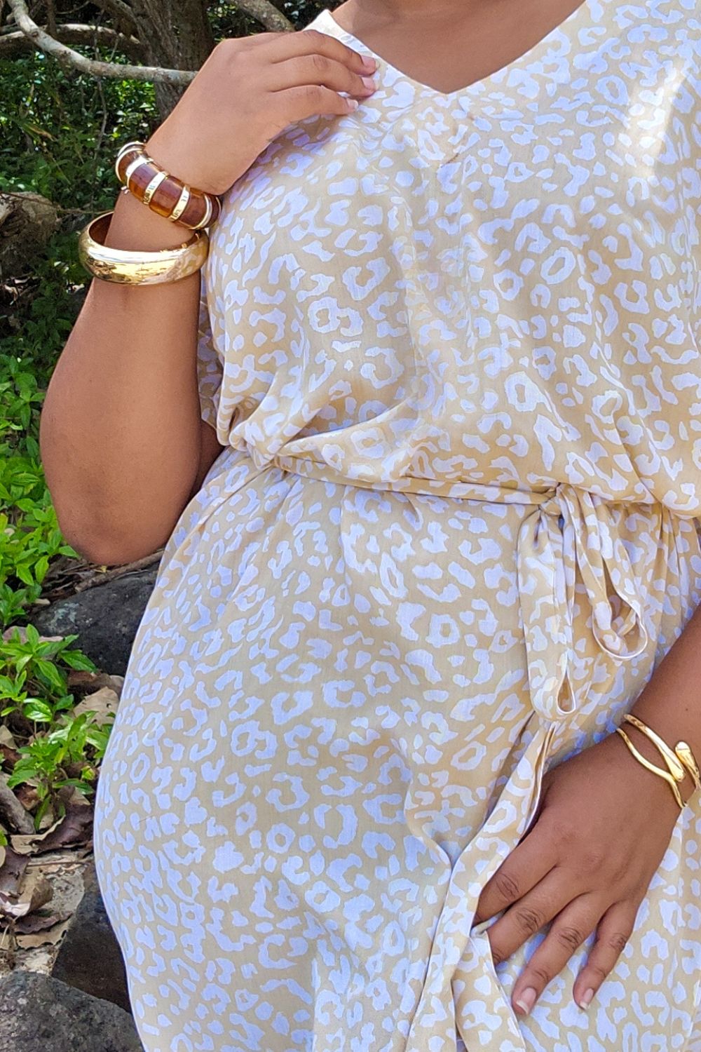 Woman wearing a beige and white leopard print long summer dress with gold accessories outdoors.